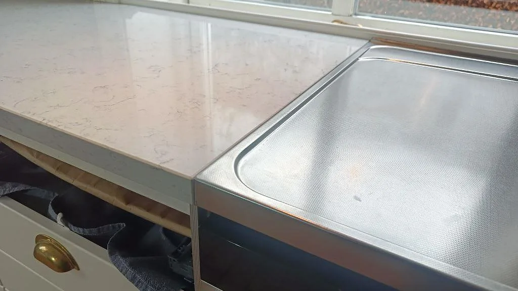 Närbild på polerad Technistone Noble Carrara bänkskiva vid rostfri spis i ett kök i Växjö.