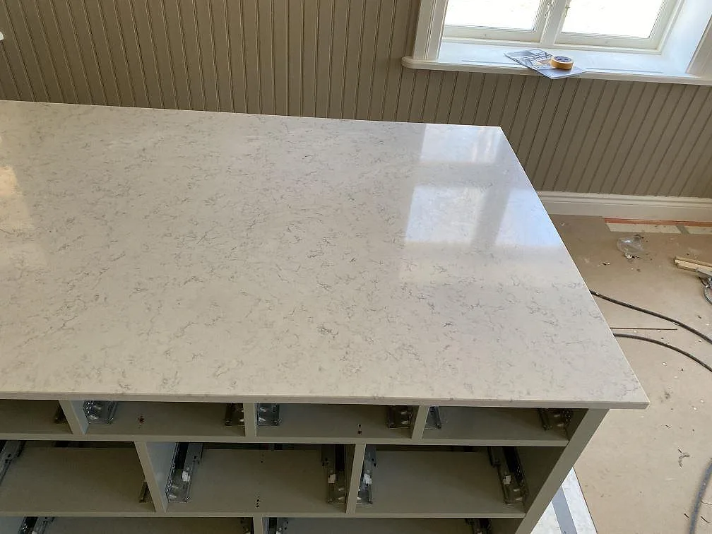 Köksö i ljus Technistone Noble Carrara, polerad kvartskomposit med marmorlik ådring, i ett kök under montering i Vaggeryd.