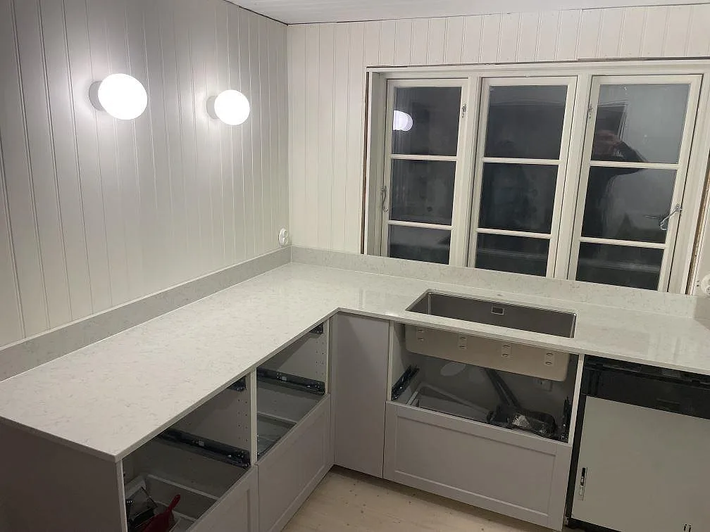 Köksbänkskiva i Technistone Noble Carrara, polerad kvartskomposit i marmorlook, med underlimmad rostfri diskho i ett L-format kök i Vallda.