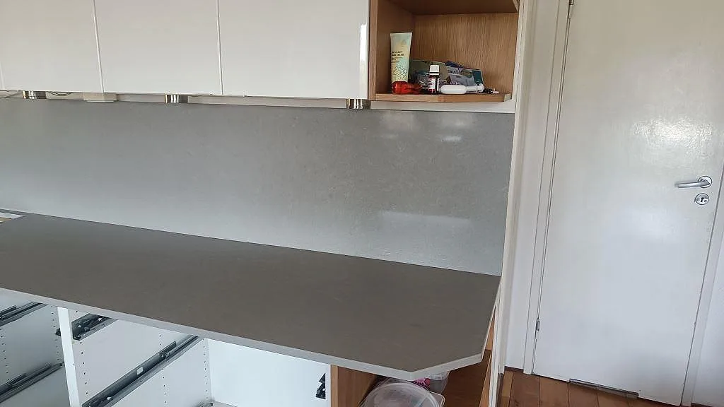 Lång köksbänkskiva i Technistone Noble Concrete Grey komposit med matchande grå stänkskydd och vita överskåp i Asmundtorp.