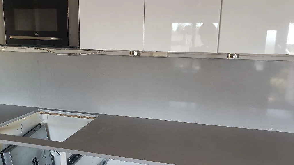 Grå Technistone Noble Concrete Grey bänkskiva med blankt stänkskydd under vita överskåp i ett kök i Asmundtorp.