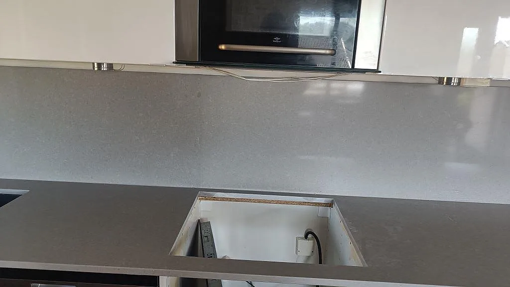 Köksbänk i Technistone Noble Concrete Grey komposit med öppen stomme och matchande stänkskydd under montering i Asmundtorp.