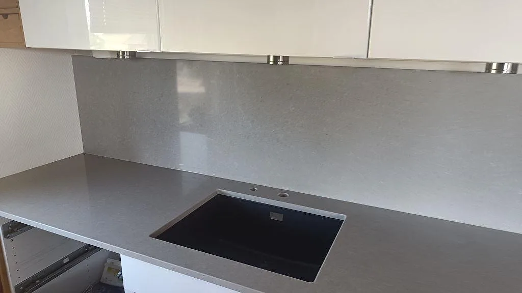 Köksbänkskiva i Technistone Noble Concrete Grey komposit med mörk diskho, kranhål och högt grått stänkskydd i Asmundtorp.