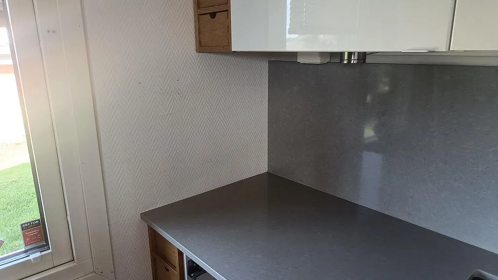 Sidovy av Technistone Noble Concrete Grey köksbänkskiva med grå stänkskyddspanel vid fönster och vit inredning i Asmundtorp.