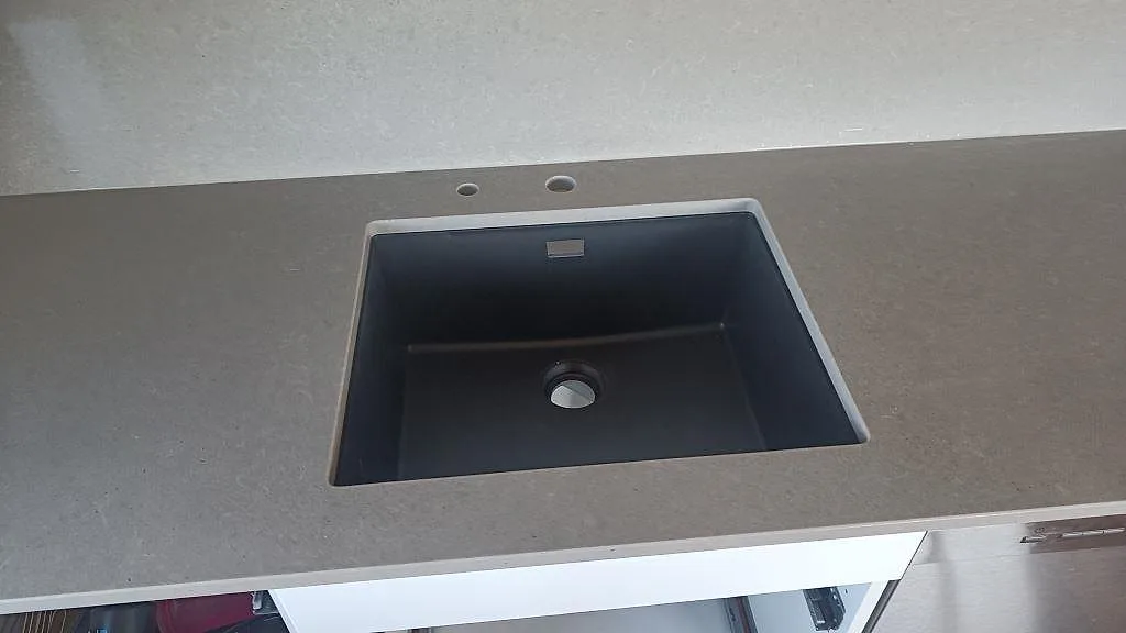 Närbild på mörk diskho i en grå Technistone Noble Concrete Grey köksbänkskiva, 20 mm komposit, i Asmundtorp.