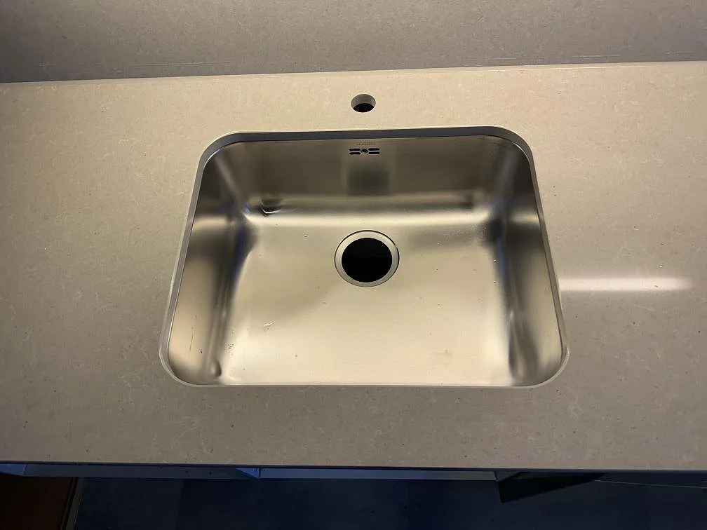 Detalj av underlimmad rostfri diskho i polerad Technistone Noble Concrete Grey med hål för blandare i Båstad.