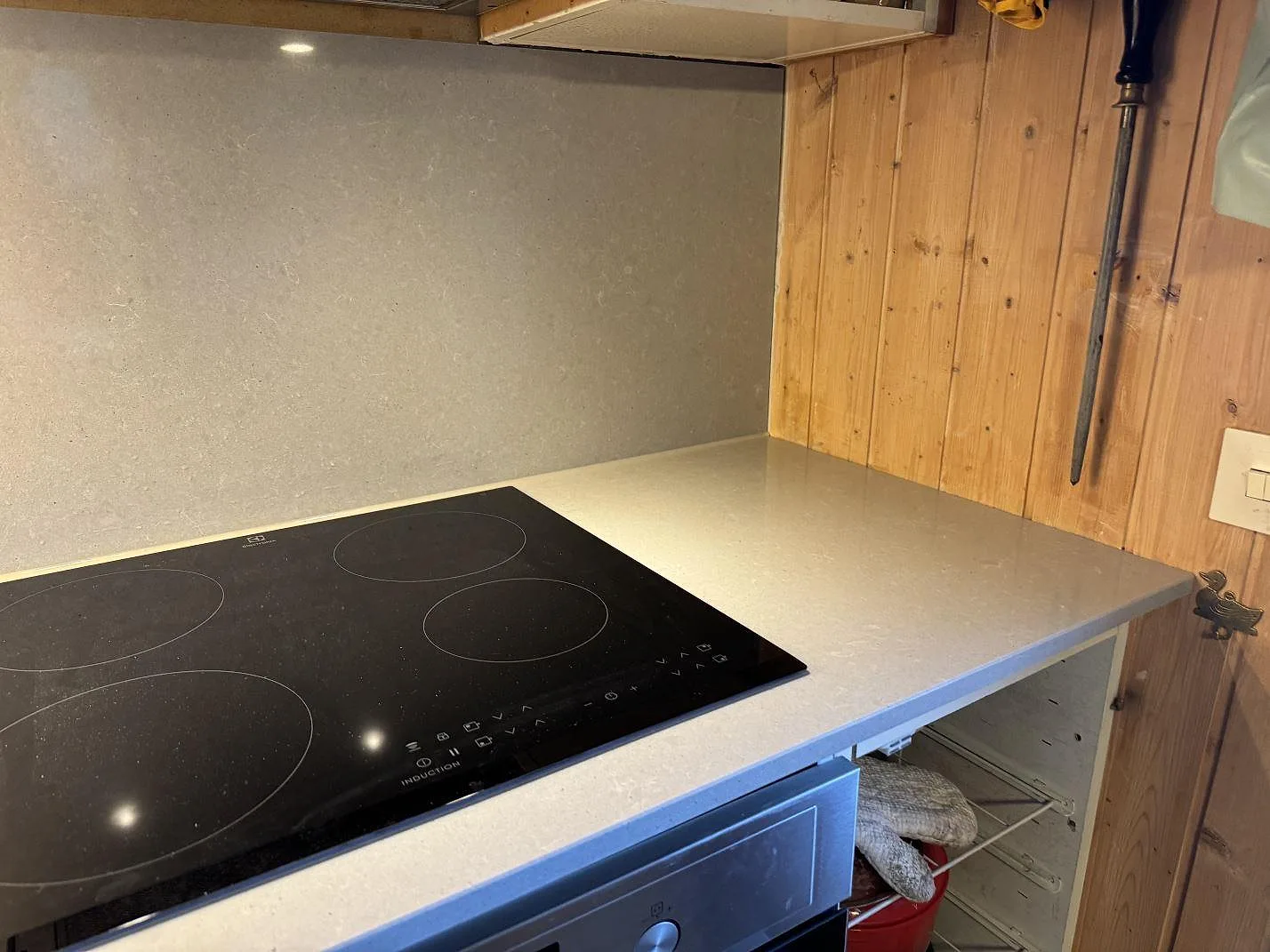 Hörndetalj med induktionshäll i polerad Technistone Noble Concrete Grey, kvartskomposit, intill trävägg i Båstad.