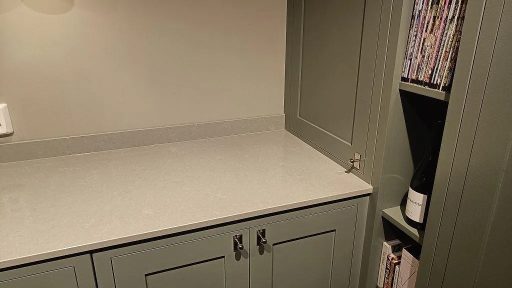 Närbild av polerad Technistone Noble Concrete Grey bänkskiva i Bankeryd, med låg stänklist och grå köksinredning intill ett öppet hyllparti.