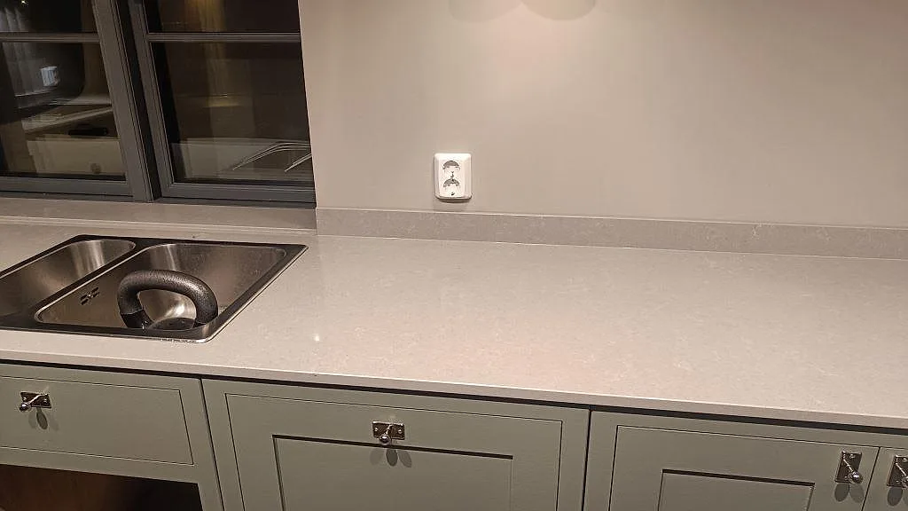 Polerad köksbänkskiva i Technistone Noble Concrete Grey i Bankeryd, med rostfri diskho och ljusgrå arbetsyta under fönster.