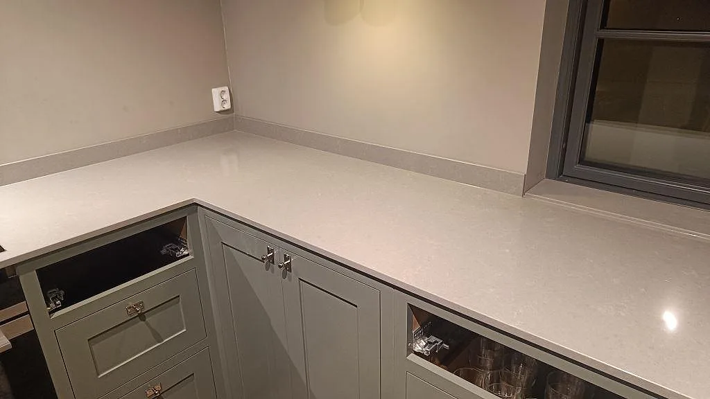 Hörnparti med polerad Technistone Noble Concrete Grey köksbänkskiva i Bankeryd, ljusgrå komposit och matchande stänklist.