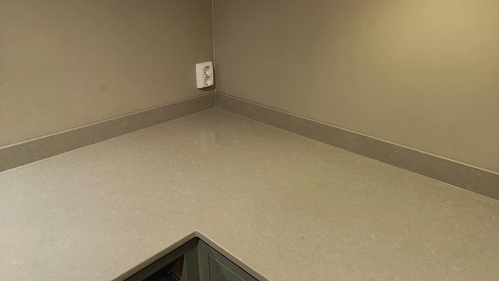Detalj av polerad Technistone Noble Concrete Grey bänkskiva i Bankeryd, med låg stänklist och betonggrå kompositstruktur i hörnet.