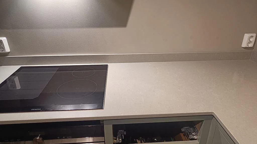 Hällsida med polerad Technistone Noble Concrete Grey köksbänkskiva i Bankeryd, låg stänklist och mörk induktionshäll.