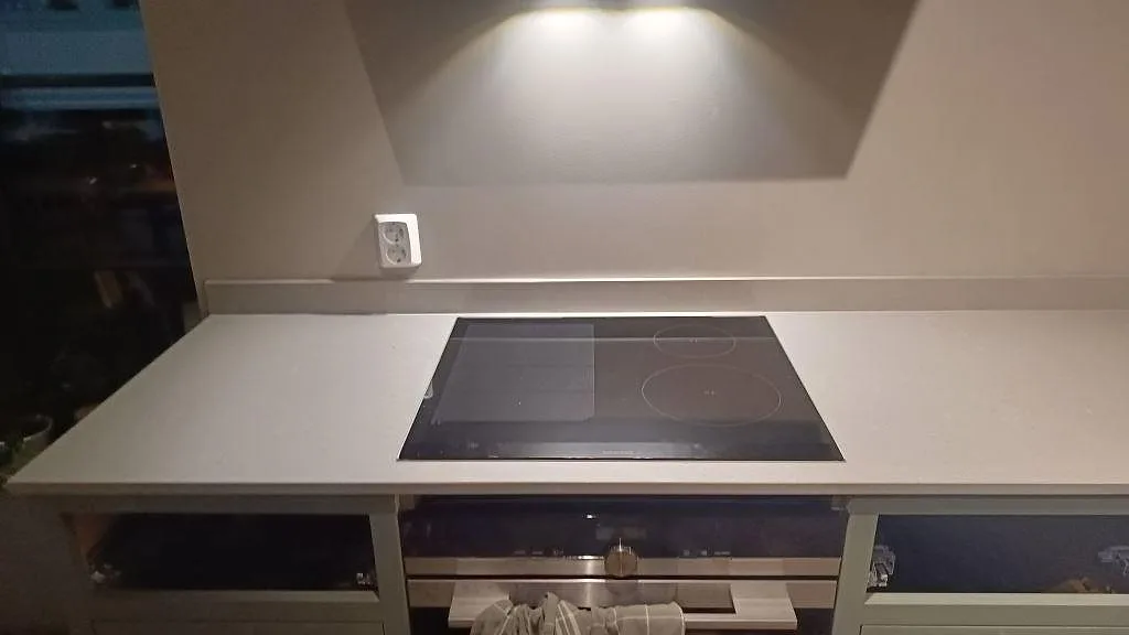 Polerad Technistone Noble Concrete Grey bänkskiva i Bankeryd under fläkt, med installerad häll och ljusgrå kvartskomposit runtom.