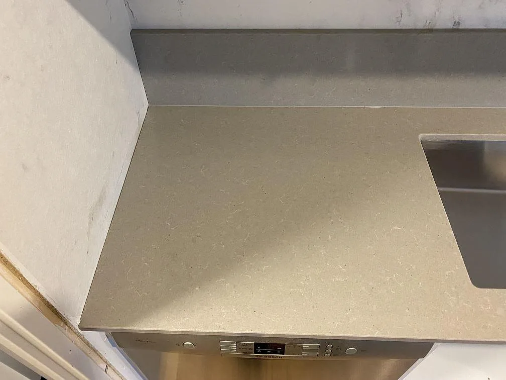 Närbild på polerad grå Technistone Noble Concrete Grey bänkskiva med låg stänkkant och diskho vid kanten i ett kök i Beddingestrand.
