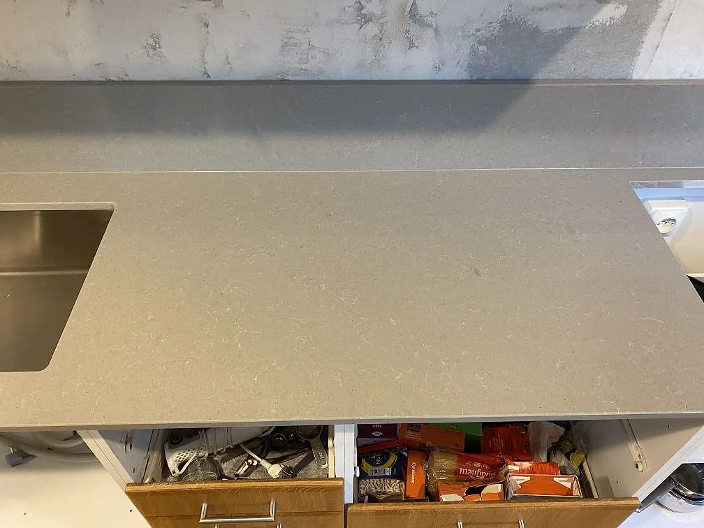 Lång arbetsyta i polerad Technistone Noble Concrete Grey, grå kvartskomposit, med diskho och låg stänkkant i ett kök under montering i Beddingestrand.
