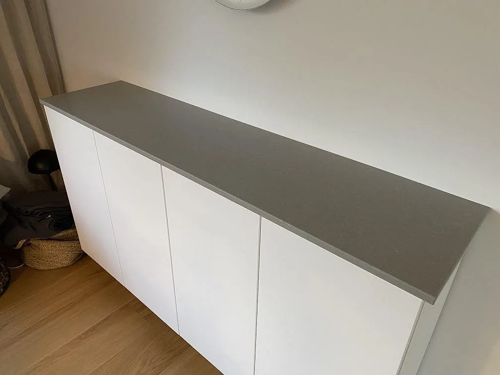 Lång skänkskiva i polerad Technistone Noble Concrete Grey på vit förvaring i ett hem i Beddingestrand.