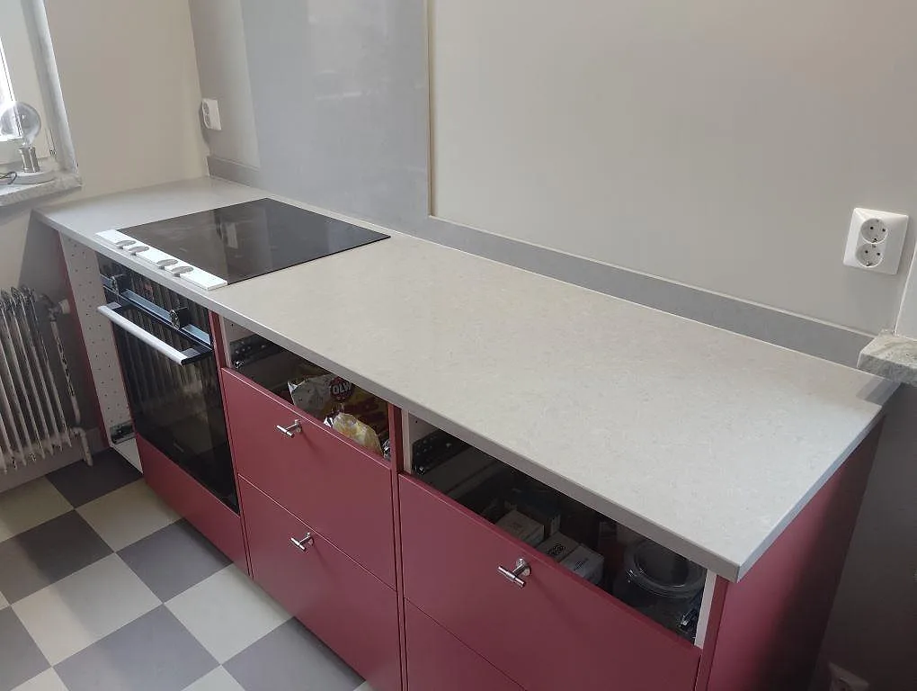 Köksbänkskiva i Technistone Noble Concrete Grey, polerad kvartskomposit, med låg stänkkant och spis i ett kök i Bromma.