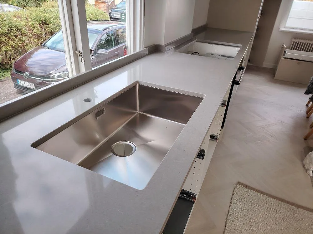 Köksbänkskiva i Technistone Noble Concrete Grey, polerad komposit, med underlimmad rostfri diskho och uppvikt stänkkant i ett kök i Bromma.