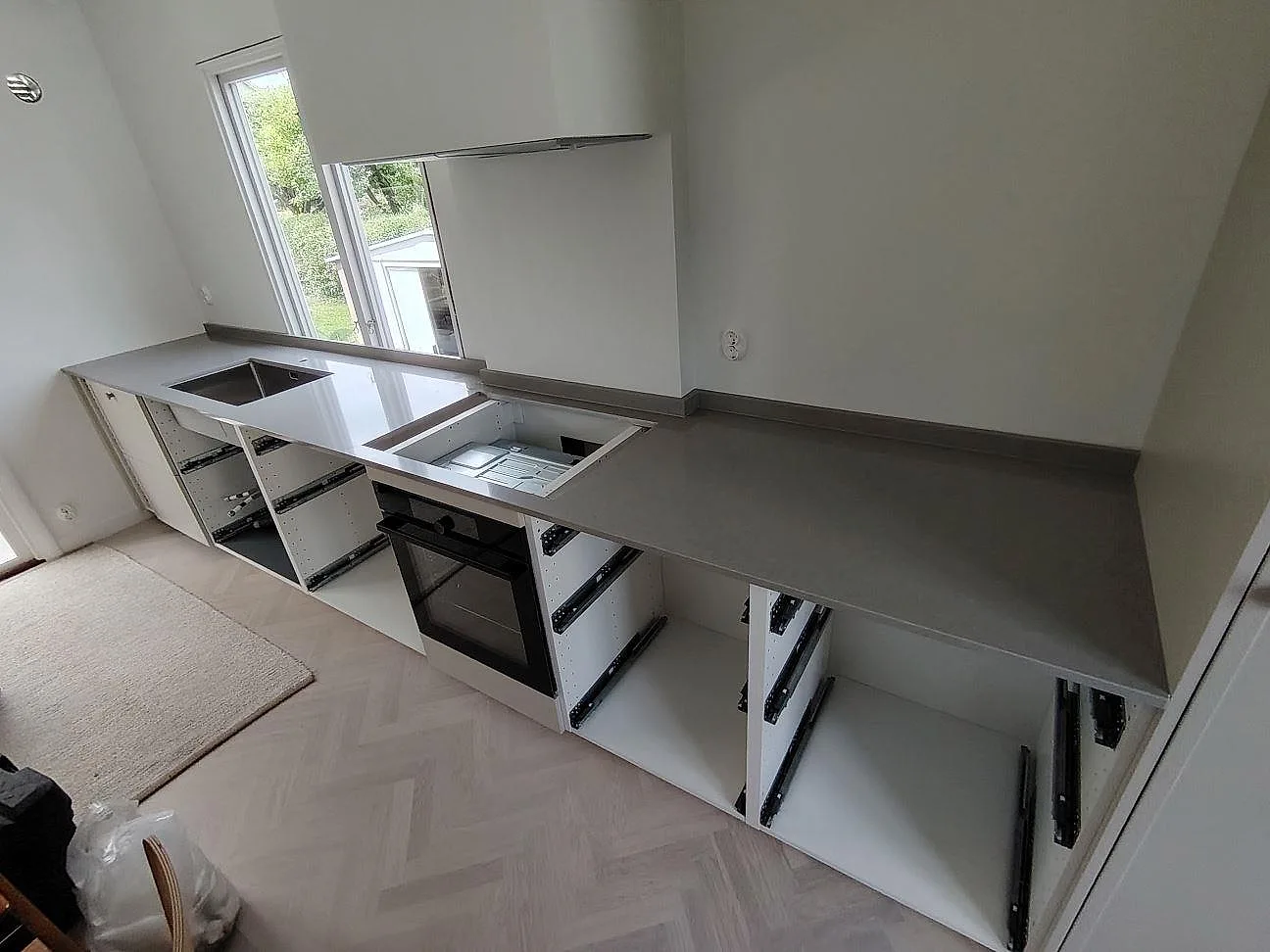 L-formad köksbänkskiva i polerad Technistone Noble Concrete Grey med hällöppning och stänkkant under montering i Bromma.