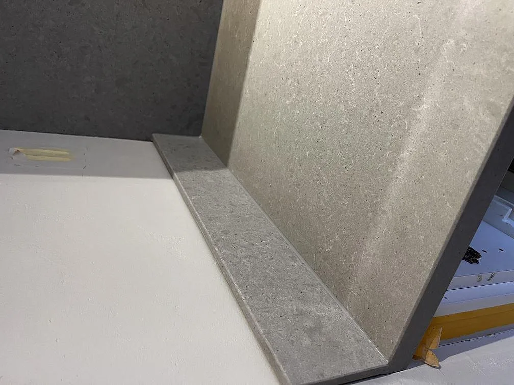 Detalj av uppvikt stänkkant i matt Technistone Noble Concrete Grey mot bänkskivan, ljusgrå betongyta, kök i Göteborg.