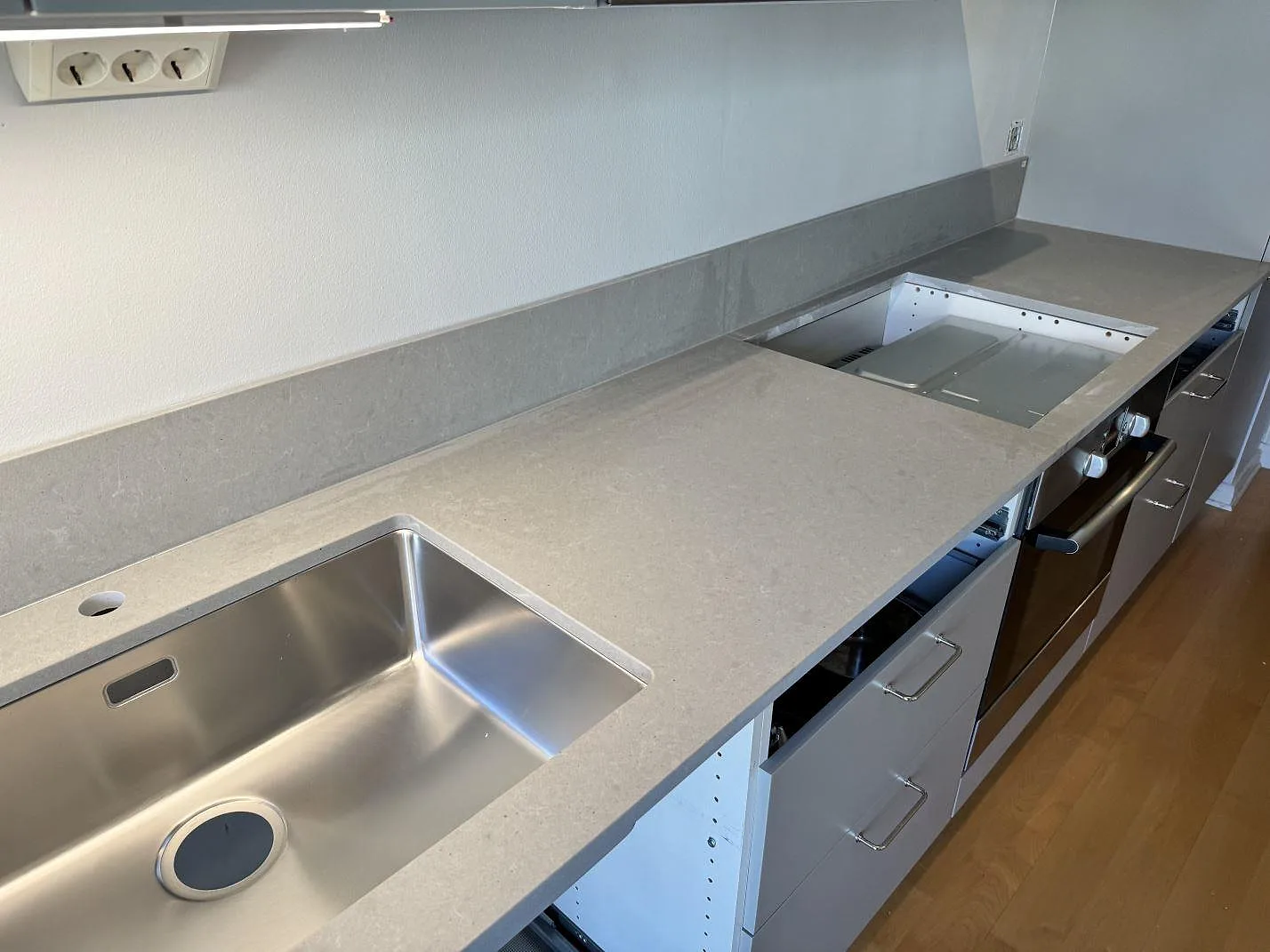 Lång köksbänkskiva i matt Technistone Noble Concrete Grey med rostfri diskho, hällöppning och uppvikt stänkkant i Göteborg.