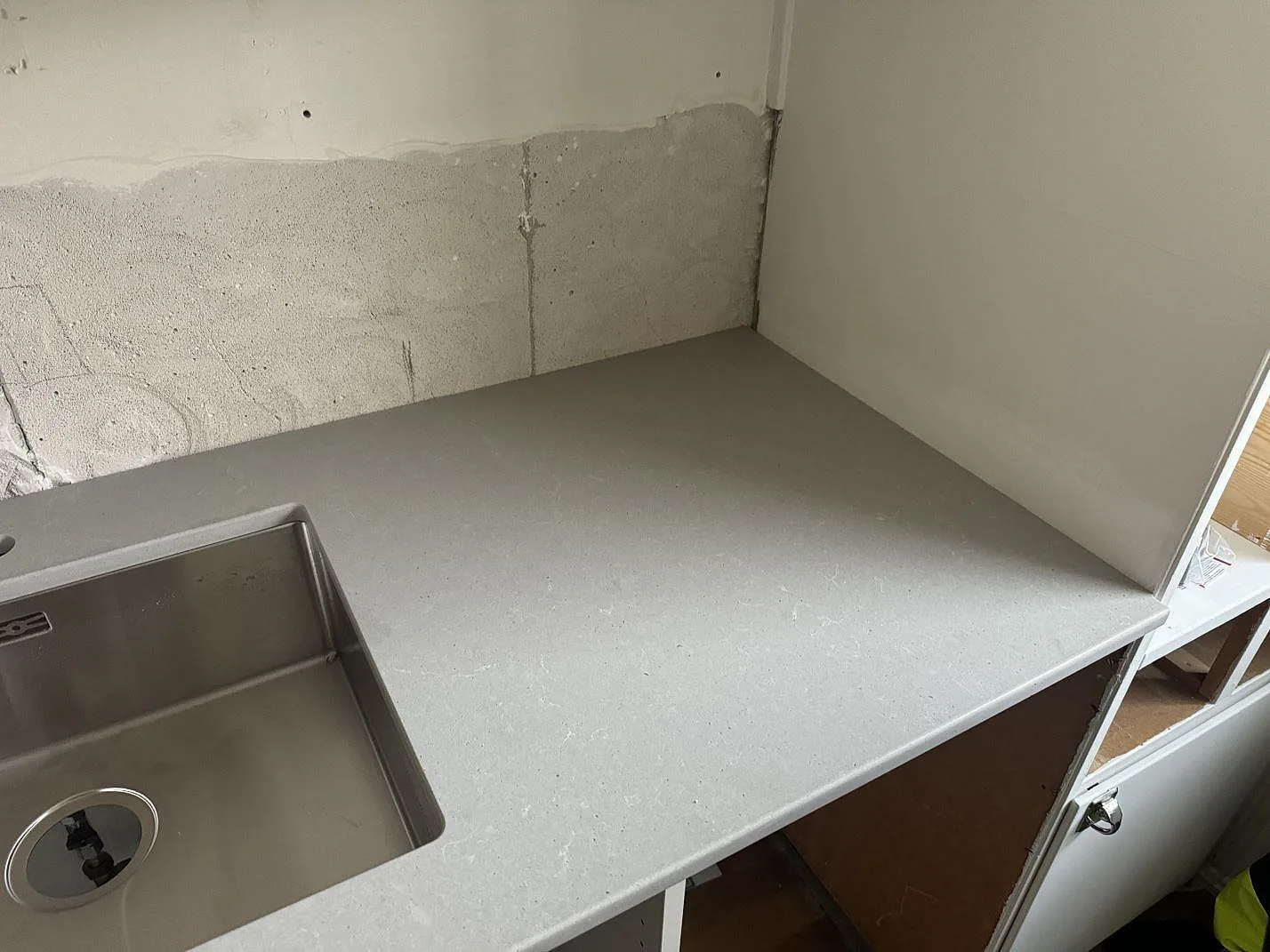 Installerad köksbänkskiva i Technistone Noble Concrete Grey, matt grå komposit, med rostfri diskho och rå väggyta i Göteborg.