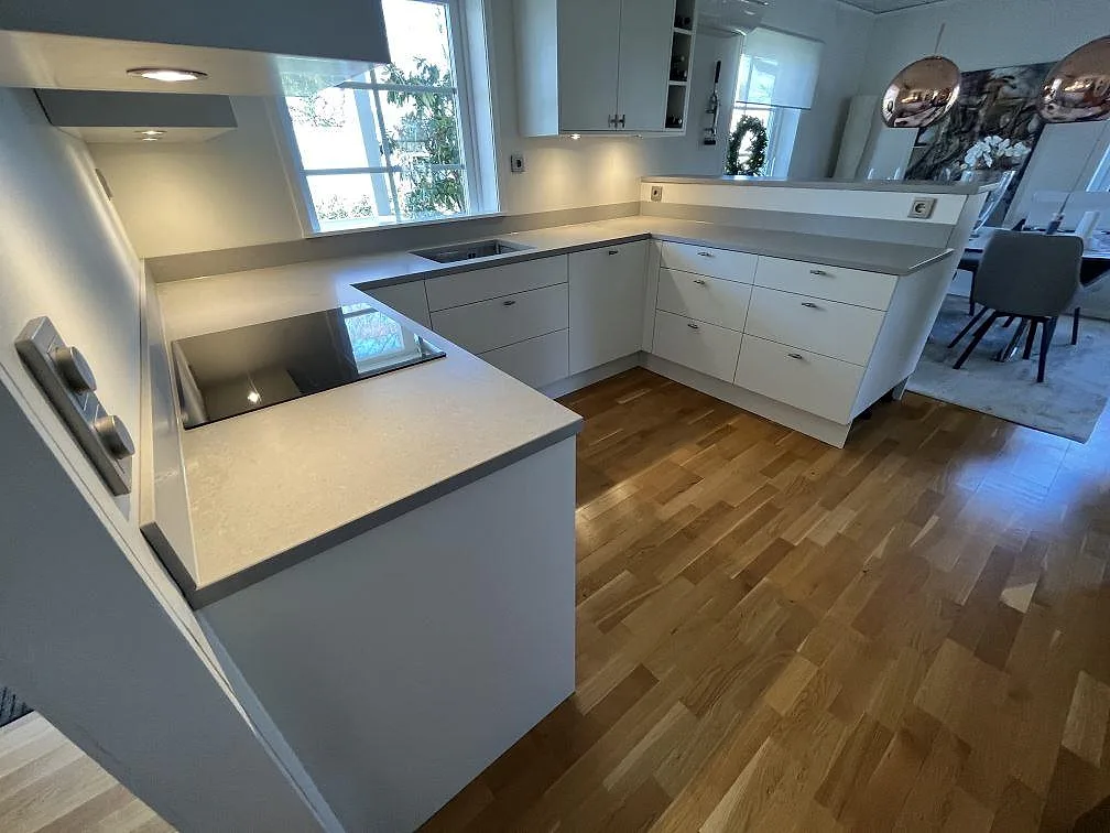 Närbild på matt Technistone Noble Concrete Grey som köksbänkskiva med låg stänkkant och synlig häll i ett vitt kök i Handen.