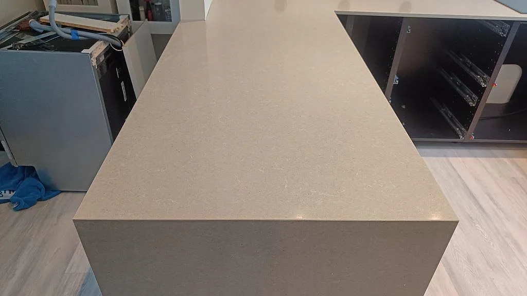 Närbild på den polerade kompositbänkskivan Technistone Noble Concrete Grey över halvön med synlig ljus struktur i Höllviken.