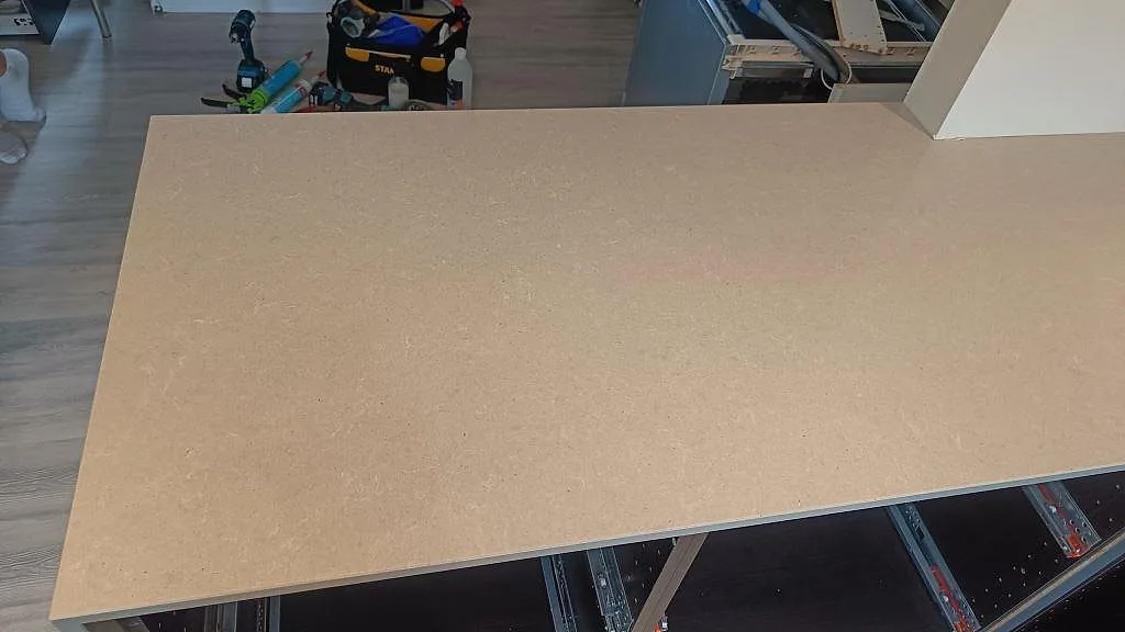 Topvy över den ljusgrå köksbänkskivan i Technistone Noble Concrete Grey på halvön med öppna köksstommar under montering i Höllviken.