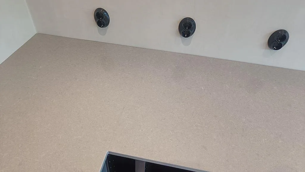 Rak detaljbild av Technistone Noble Concrete Grey, polerad komposit, längs väggsidan med eluttag ovanför bänkskivan i Höllviken.