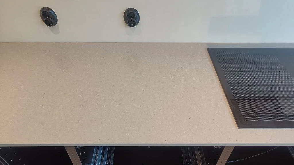 Köksbänkskiva i polerad Technistone Noble Concrete Grey med svart induktionshäll och ljus vägg i ett kök i Höllviken.