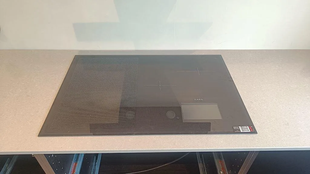Närbild på svart induktionshäll monterad i polerad Technistone Noble Concrete Grey, ljus kompositbänkskiva i Höllviken.