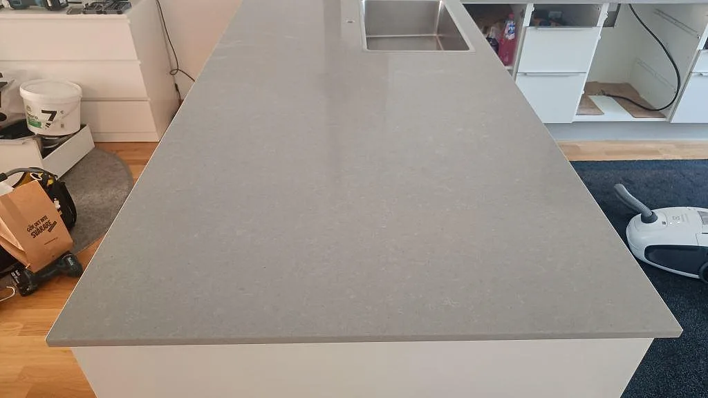 Polerad köksbänkskiva i Technistone Noble Concrete Grey komposit över en halvö med rostfri diskho i ett kök i Jönköping.