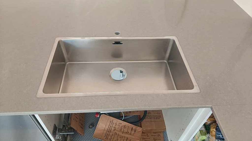 Rostfri diskho monterad under en polerad Technistone Noble Concrete Grey bänkskiva i ett kök under montering i Jönköping.
