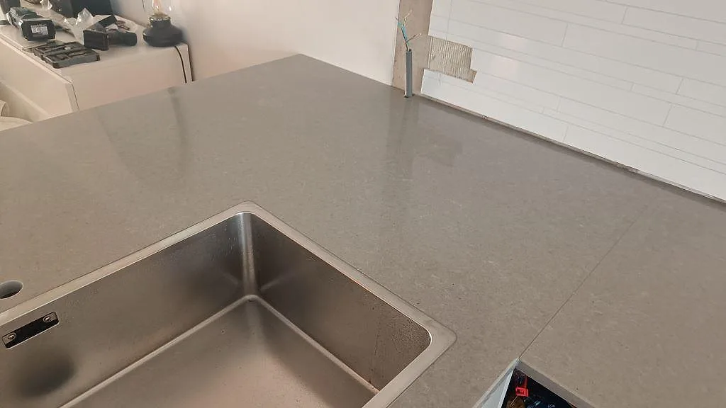 Köksbänkskiva i grå Technistone Noble Concrete Grey komposit vid diskho och vit kakelvägg i Jönköping.