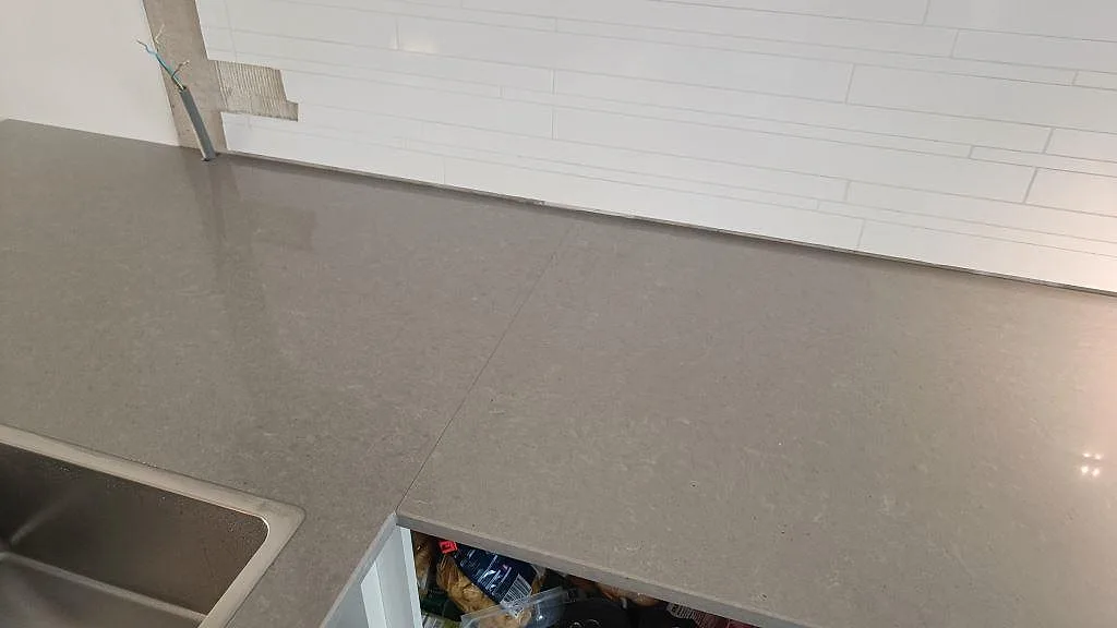Detalj av polerad Technistone Noble Concrete Grey bänkskiva längs vit kakelvägg i ett kök i Jönköping.