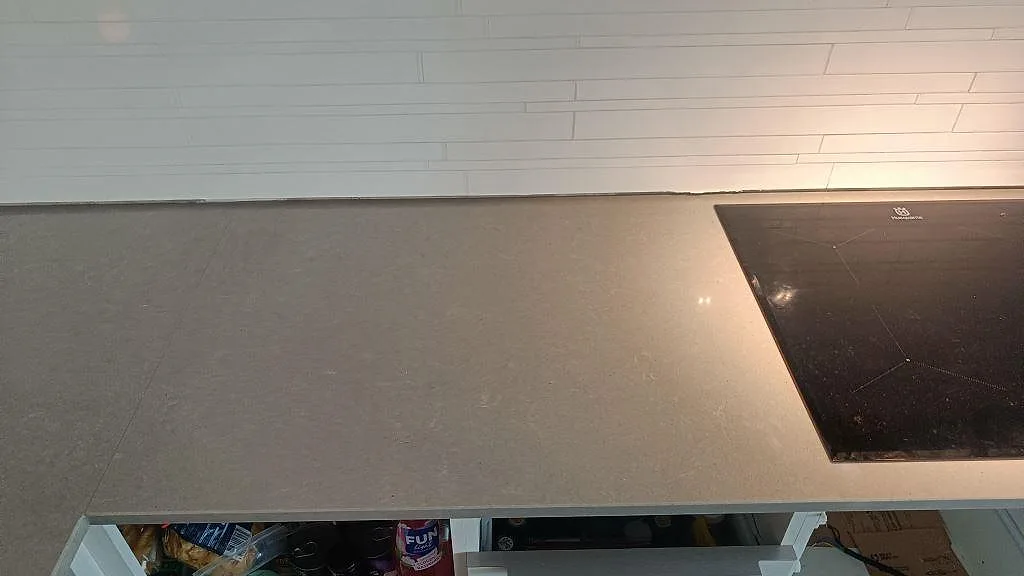 Köksbänk i Technistone Noble Concrete Grey komposit med svart induktionshäll och vit kakelvägg i Jönköping.