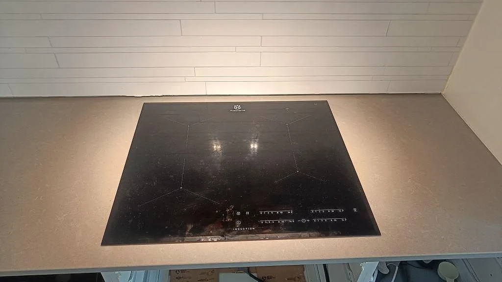 Svart induktionshäll i en polerad Technistone Noble Concrete Grey köksbänkskiva med vit kakelvägg i Jönköping.
