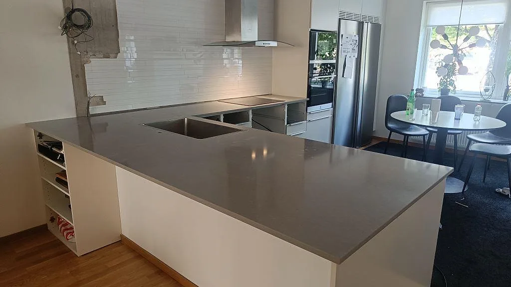 L-formad köksbänkskiva i polerad Technistone Noble Concrete Grey komposit med halvö, rostfri diskho och svart induktionshäll i Jönköping.