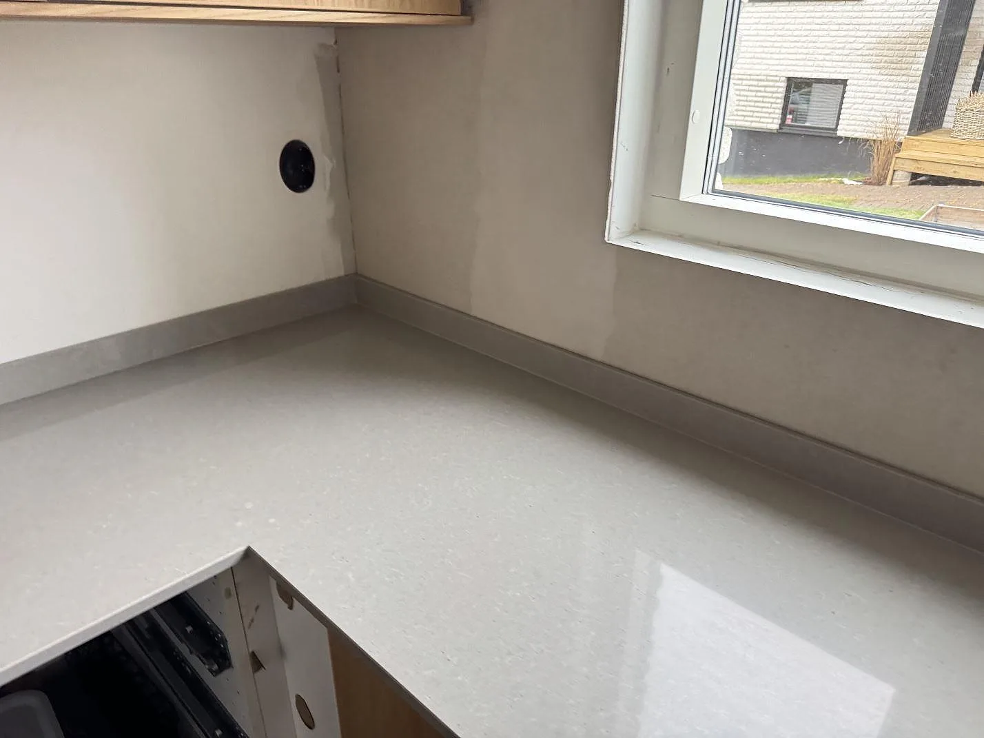 Polerad köksbänk i Technistone Noble Concrete Grey i hörnet under ett fönster med låg stänkkant i ett kök i Jönköping.