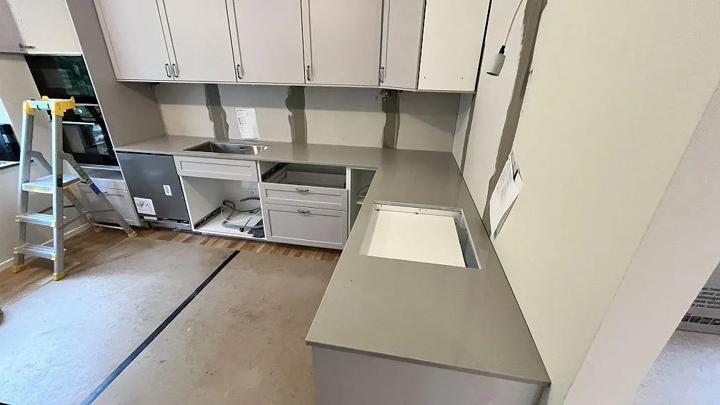 Polerad kvartskompositskiva i Technistone Noble Concrete Grey med öppning i arbetsytan och skyddat golv under köksmontering i Knivsta.