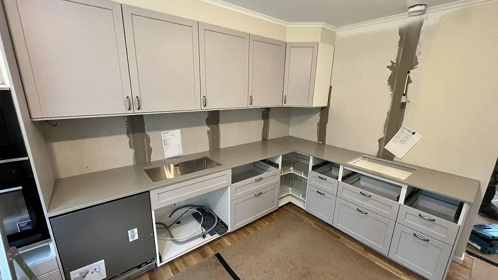L-formad köksbänkskiva i 20 mm polerad Technistone Noble Concrete Grey med synlig diskho i ett kök under montering i Knivsta.