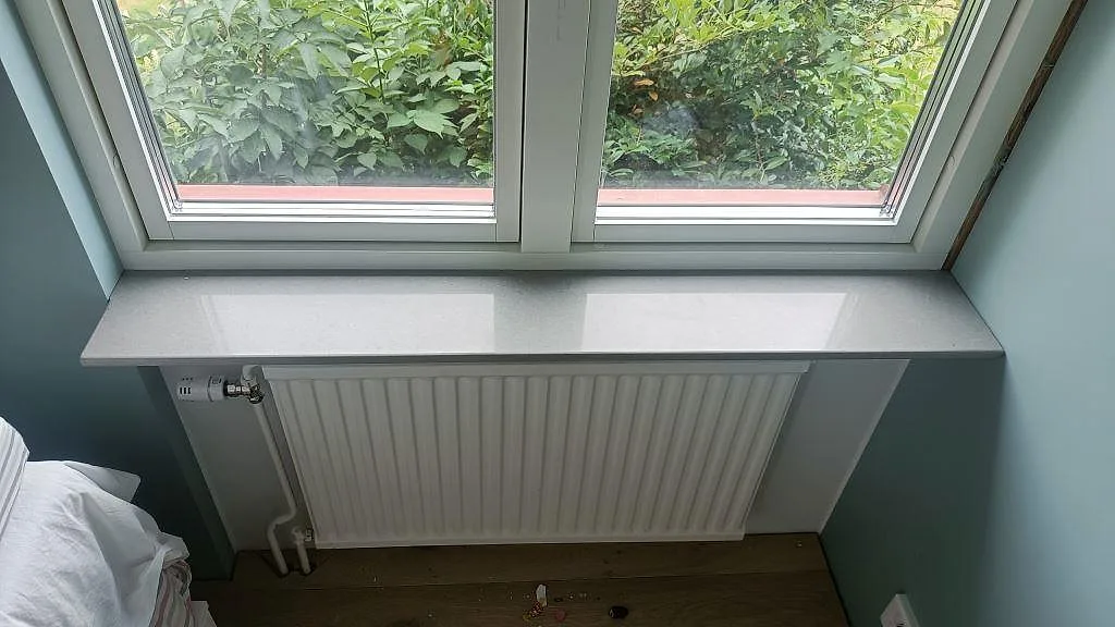 Fönsterbänk i grå Technistone Noble Concrete Grey monterad ovanför en radiator vid ett köksfönster i Kristianstad.
