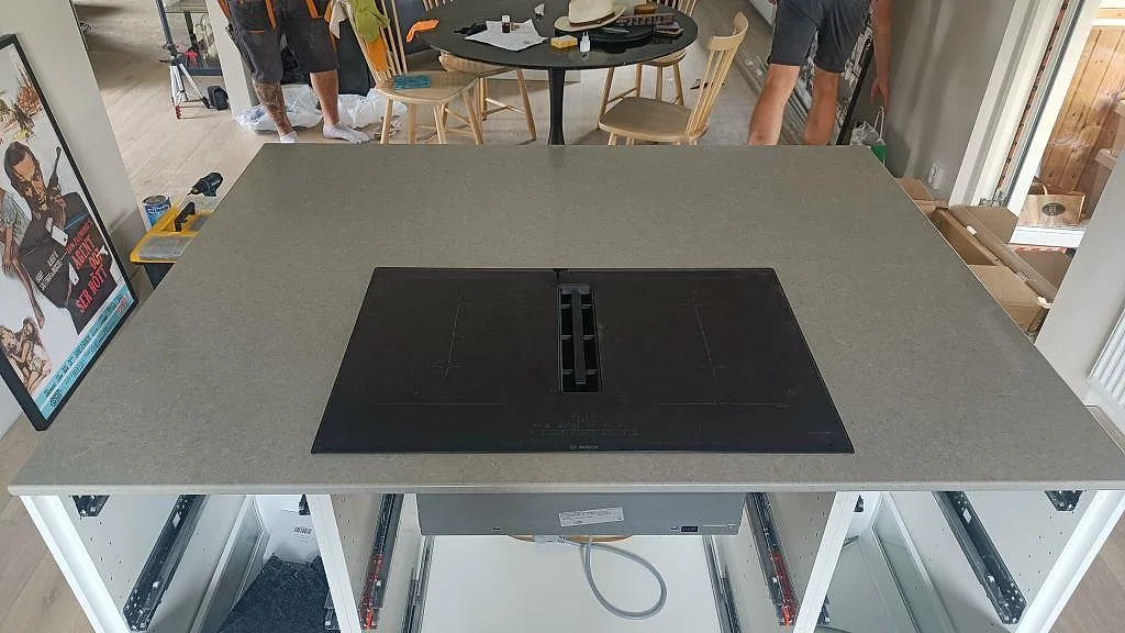 Köksö i grå Technistone Noble Concrete Grey med Bosch induktionshäll och integrerad fläkt under köksmontering i Kristianstad.