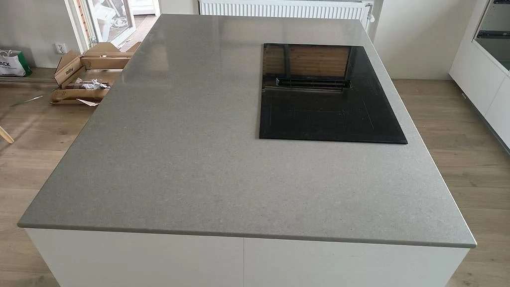Köksö i grå Technistone Noble Concrete Grey med infälld induktionshäll och integrerad fläkt, sedd snett ovanifrån i ett kök i Kristianstad.