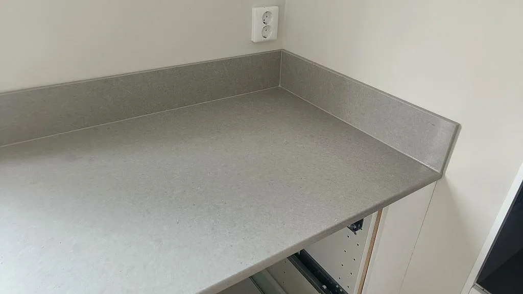 Köksbänkskiva i grå Technistone Noble Concrete Grey med uppvikt stänkkant mot väggen i ett kök i Kristianstad.