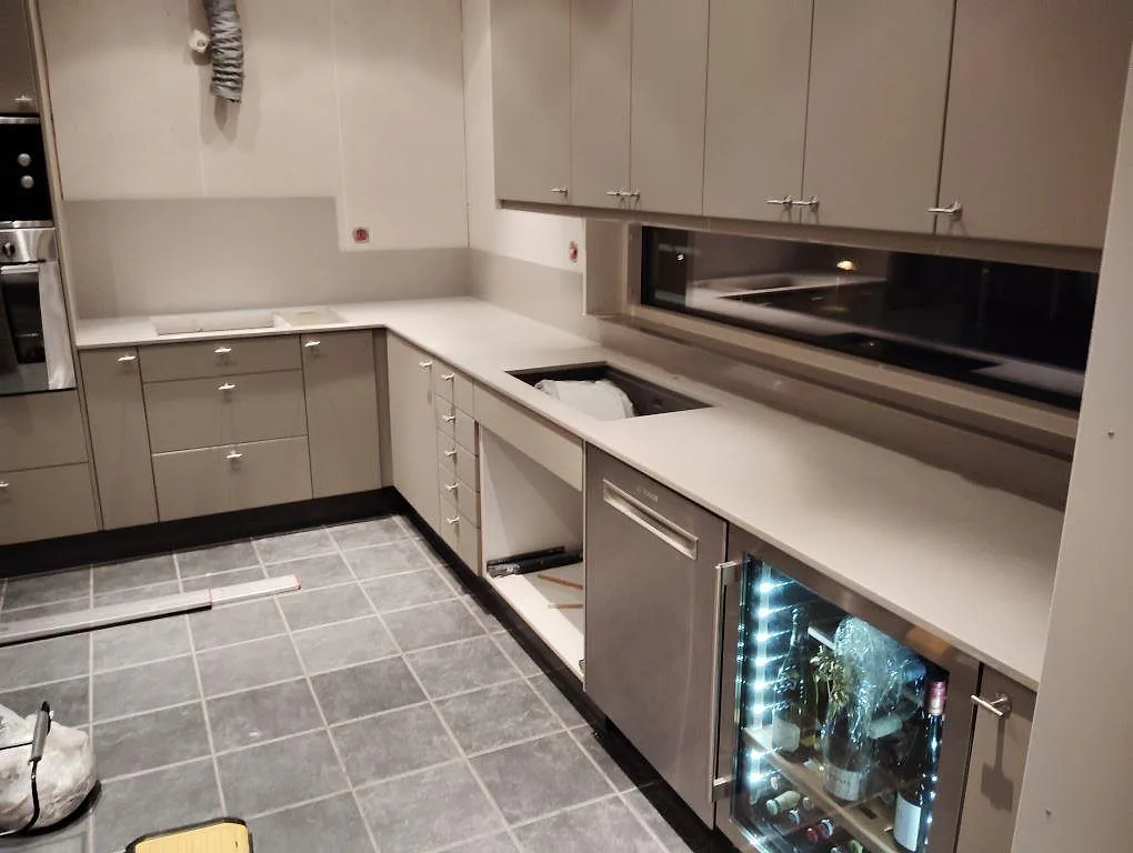 Köksbänkskiva i polerad Technistone Noble Concrete Grey med stänkskydd och öppningar för diskho och häll i ett L-kök i Lidingö.