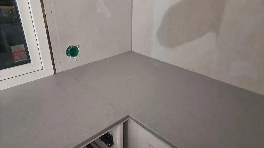 Hörnparti med matt grå köksbänkskiva i Technistone Noble Concrete Grey mot ofärdig vägg i Limhamn.