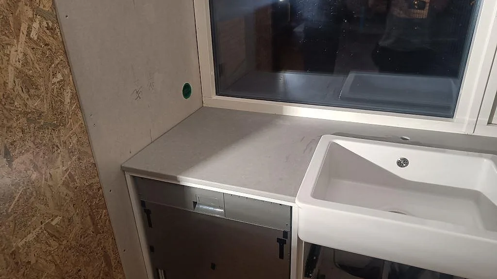 Vänstra delen av köksbänkskivan i Technistone Noble Concrete Grey, matt grå komposit, vid fönster och vit diskho i Limhamn.