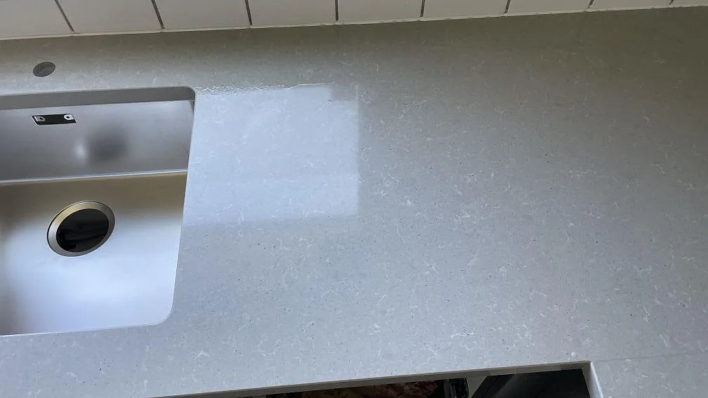 Diskhoområde och arbetsyta i polerad grå Technistone Noble Concrete Grey komposit med vitt kakel bakom i ett kök i Limhamn.